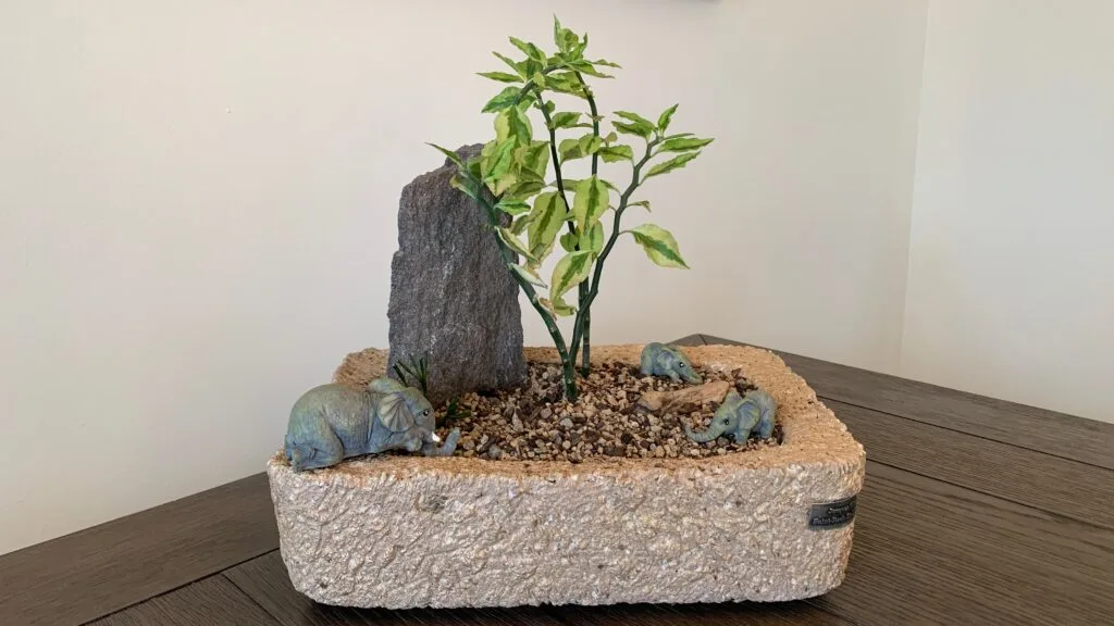 Handcrafted hypertufa pot with a tall stone, a variegated plant, and miniature hippos, sold to Sylvie D.