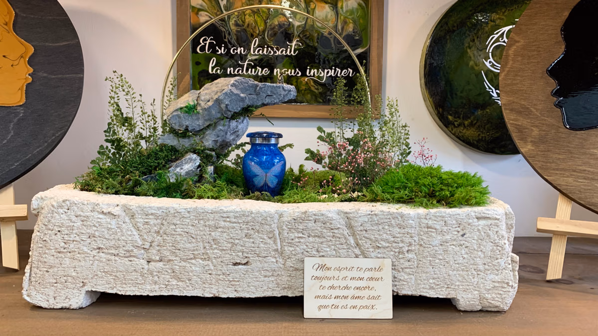 Large handcrafted hypertufa memorial planter in light stone finish, textured like a monolithic block, featuring a blue urn integrated into a natural arrangement of moss, ferns, and layered rocks.